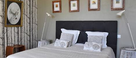 A neatly made bed with a dark headboard, white bedding, and multiple pillows. There are framed pictures on the wall above the bed.