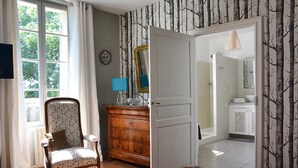 Un dormitorio con un aparador de madera, una silla, una cama y un baño visible a través de una puerta abierta.