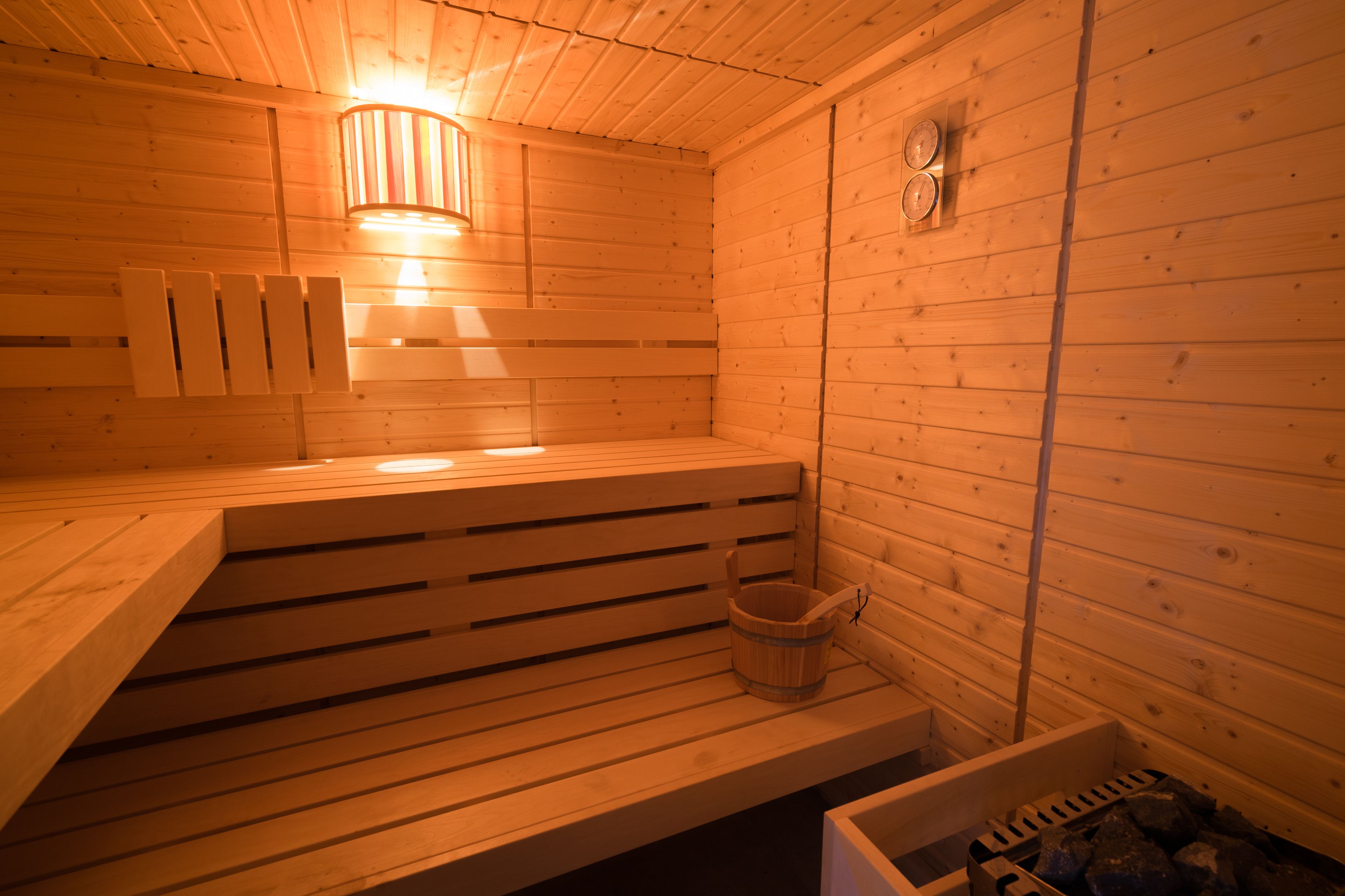 Een sauna met houten banken, een houten emmer en een heater aan de muur.