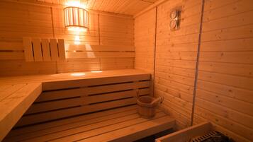 Een sauna met houten banken, een houten emmer en een heater aan de muur.