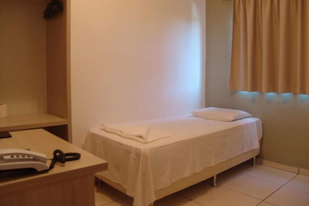 A small, single-bed room with a wooden desk and a telephone.