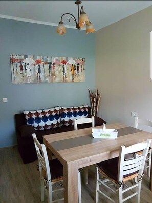 A dining area with a wooden table and chairs, a sofa with patterned cushions, and a painting on the wall. - Marathon Studios &Apartments (Zakynthos)