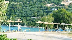 A beachside resort with sun umbrellas, lounge chairs, and a view of the sea and hills. - Marathon Studios &Apartments (Zakynthos)