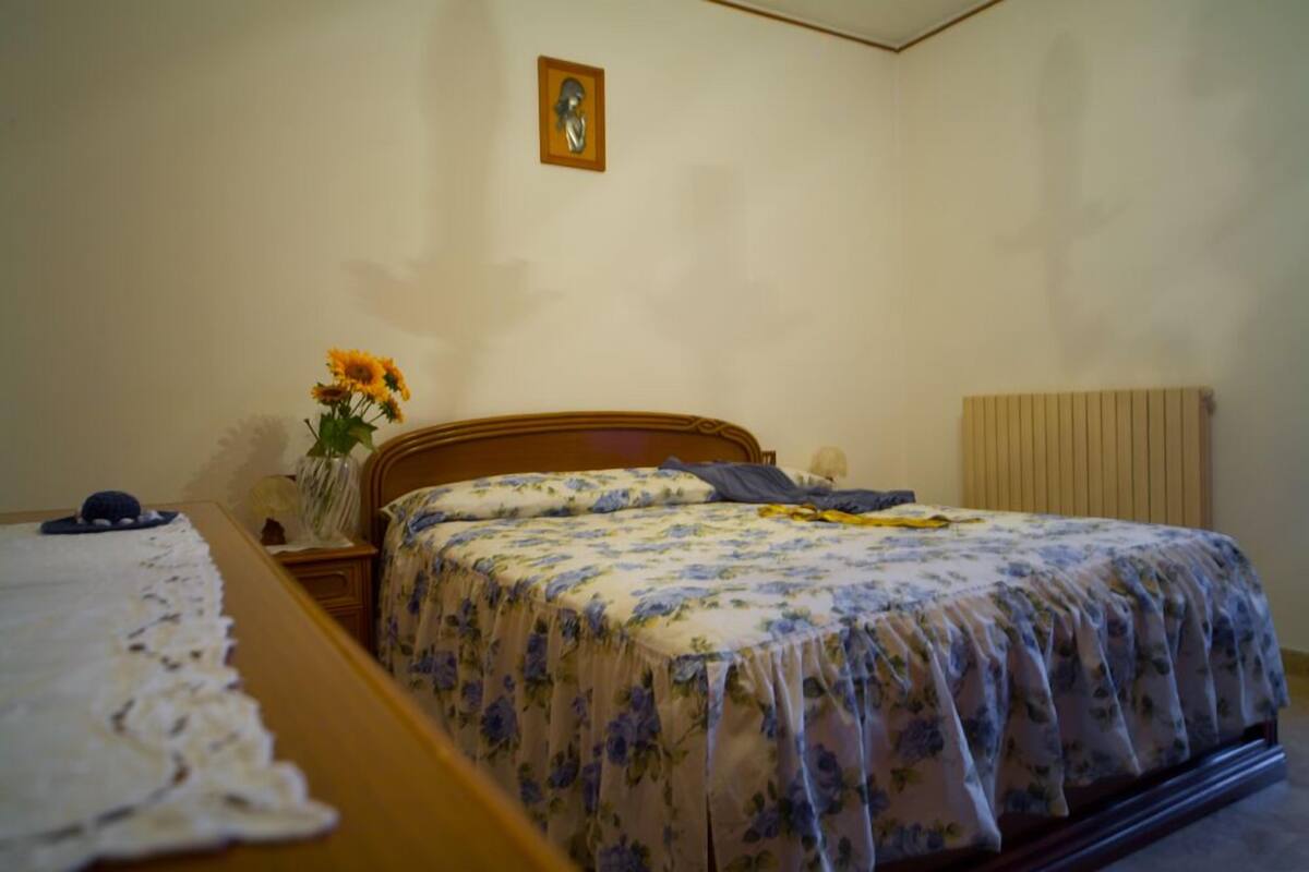 Une chambre à coucher avec un lit en bois, une table de chevet, un vase avec des fleurs et un radiateur.