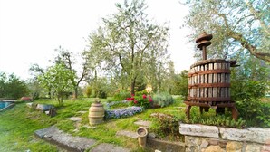 A garden with a wooden barrel fountain, a stone wall, and various plants and flowers. - Agriturismo Cognanello (Montepulciano)