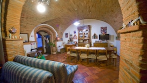 A cozy room with a brick ceiling, a dining table with chairs, a sofa, and a television on the wall. - Agriturismo Cognanello (Montepulciano)