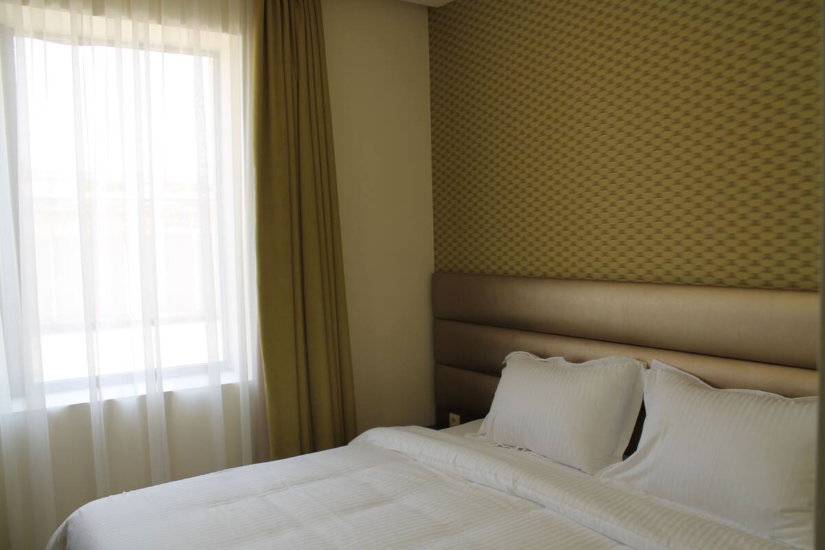 Une chambre d’hôtel avec un lit, des rideaux, un mur à motifs et une tête de lit.