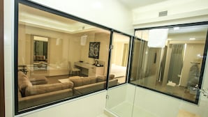 A modern hotel room with a glass partition, a sofa, a desk, and a bathroom with a shower and toilet. - Pirimze Plaza (Tbilisi)