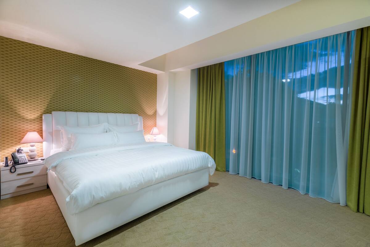 Une chambre d’hôtel avec un grand lit, une table de chevet avec une lampe, un téléphone et un mur décoré d’un motif.