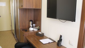 A hotel room with a wooden desk, a flat-screen TV mounted on the wall, a coffee maker, and a remote control on the desk. - Pirimze Plaza (Tbilisi)