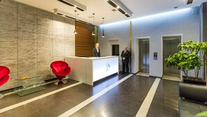 A modern reception area with a reception desk, two red chairs, a potted plant, and a glass display case. - Pirimze Plaza (Tbilisi)