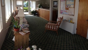 A hotel room with a wooden desk, a wicker chair, a potted plant, and a bulletin board with various notices. - Gold Crest Motel (Wildwood Crest)