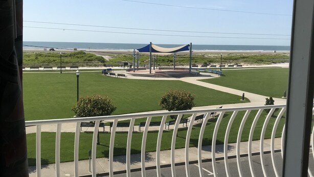 A balcony with a view of a beach, a blue canopy structure, and a red bench. - Gold Crest Motel (Wildwood Crest)