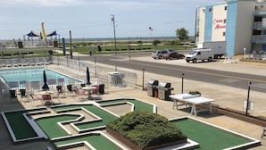A pool area with a maze, lounge chairs, and a building in the background. - Gold Crest Motel (Wildwood Crest)