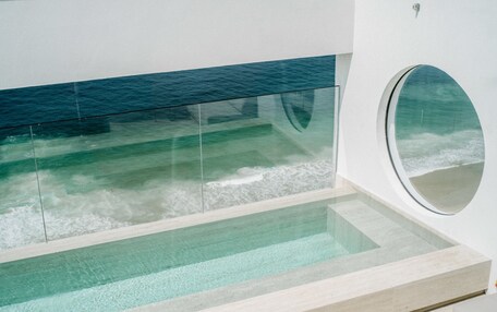 Un interior moderno con una piscina de fondo de vidrio, un ventanal circular y vista al océano.