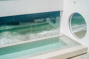 Un interior moderno con una piscina de fondo de vidrio, un ventanal circular y vista al océano.