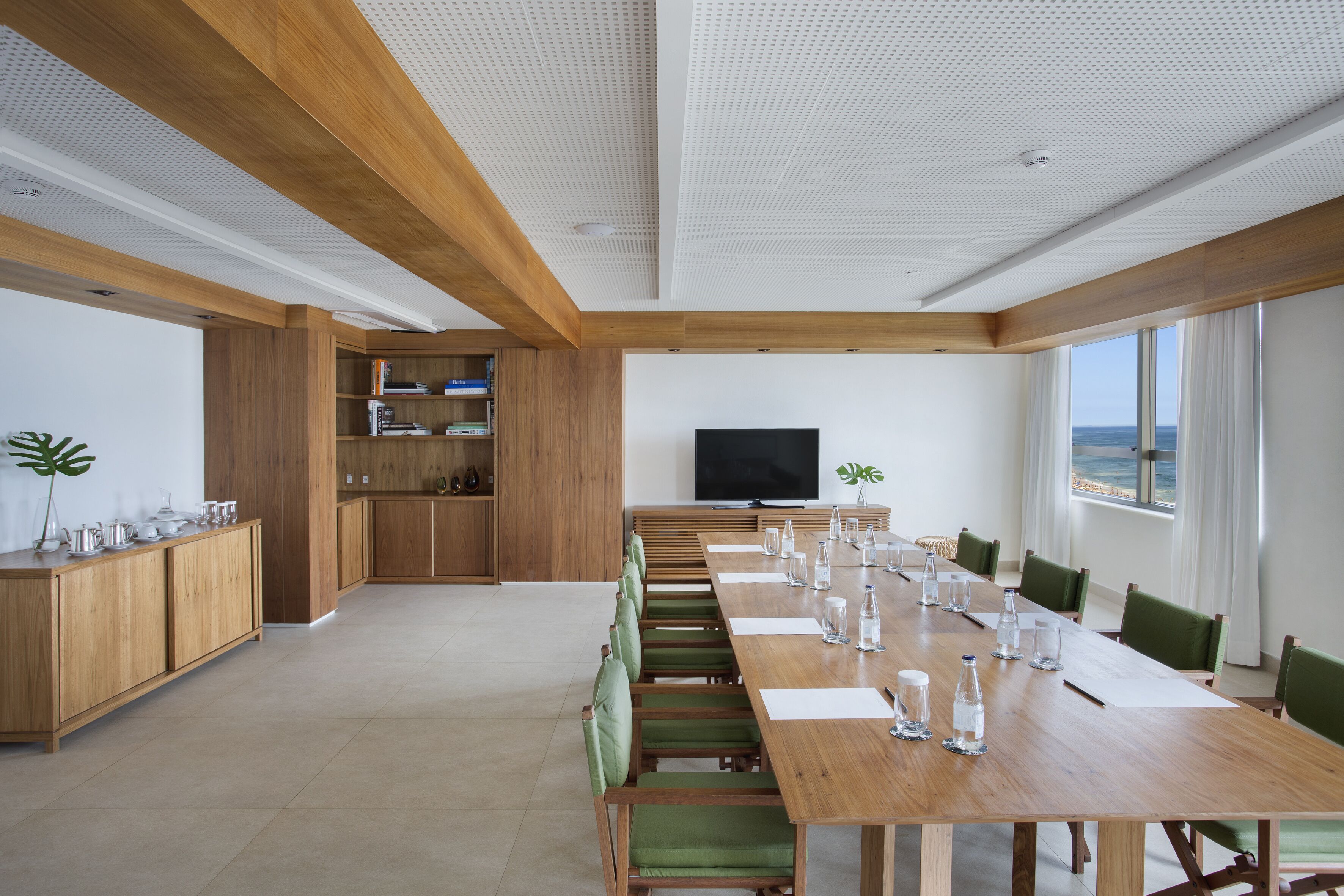 Una amplia sala de conferencias con una larga mesa de madera, sillas verdes y un televisor de pantalla plana.
