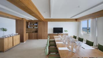 Una amplia sala de conferencias con una larga mesa de madera, sillas verdes y un televisor de pantalla plana.