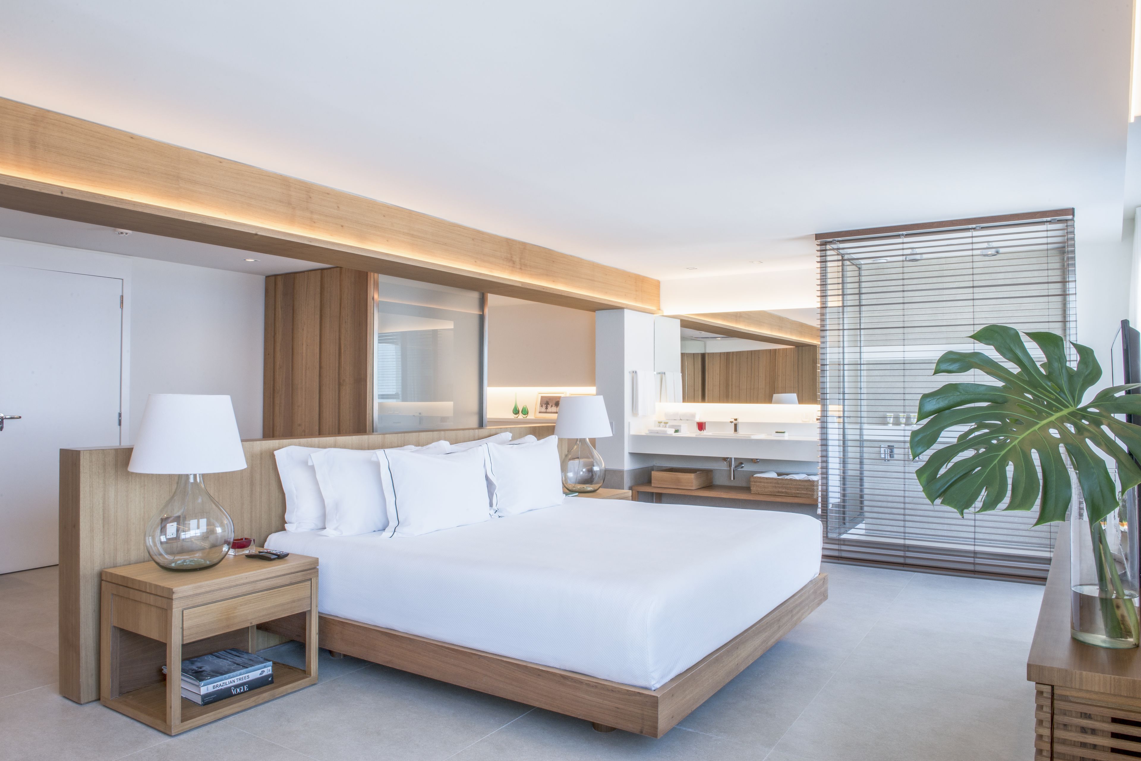 Una habitación de hotel moderna con una cama grande, mesitas de noche, un espejo, un televisor y una planta.