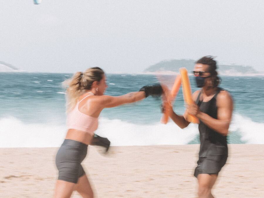 Two people practicing martial arts on a sandy beach with the ocean in the background.