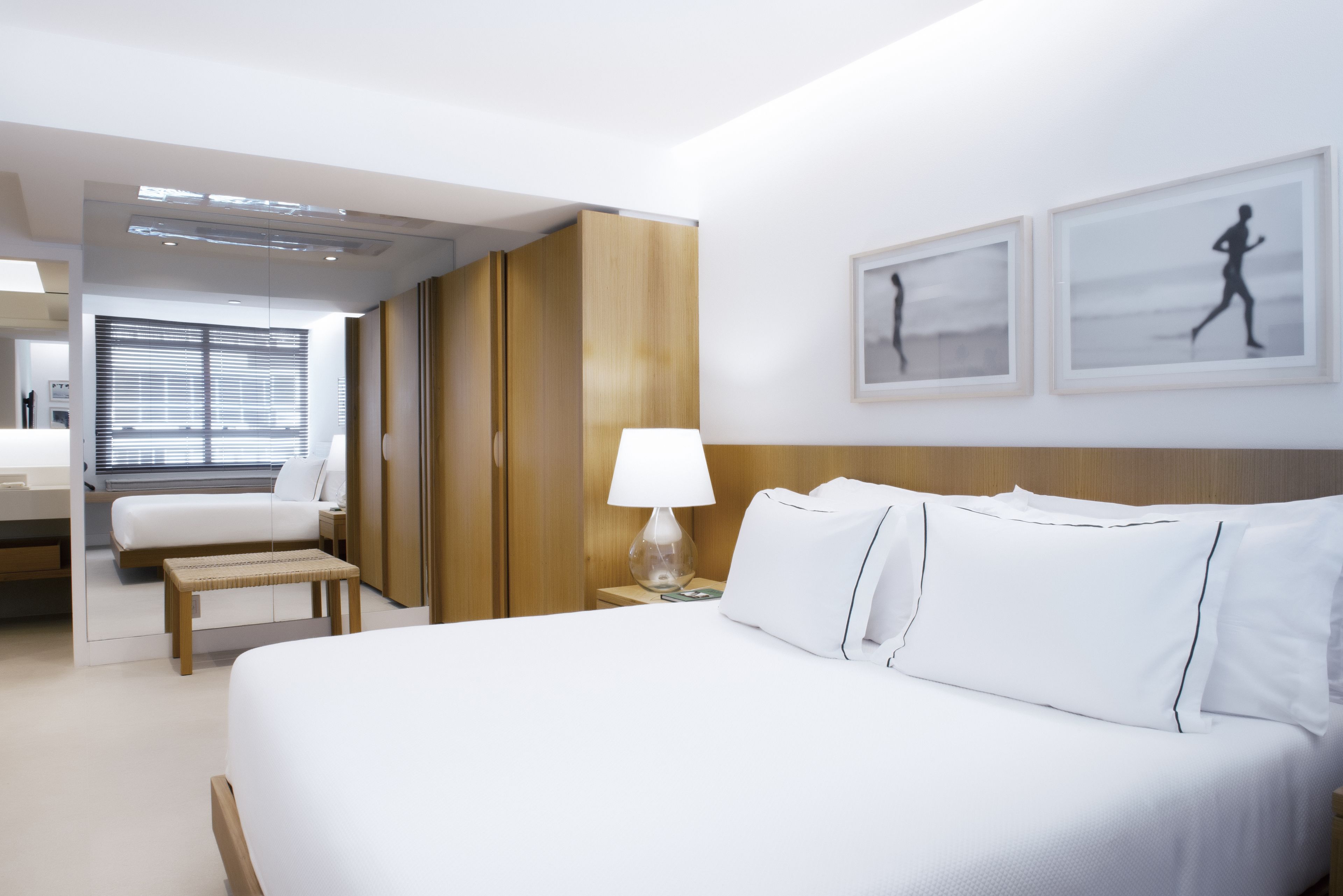 Quarto de hotel com cama grande, mesa de cabeceira, abajur e uma obra de arte na parede.