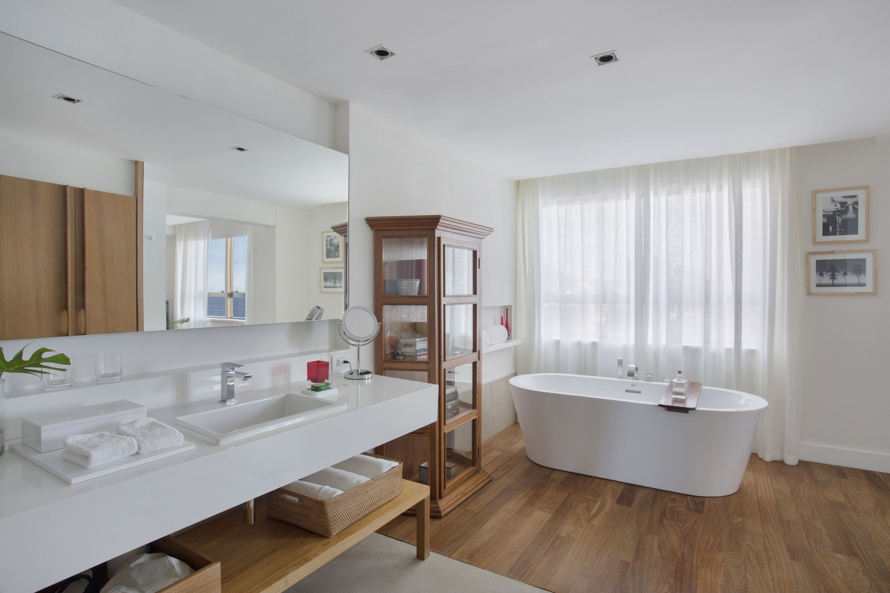 Een moderne badkamer met een vrijstaand bad, een grote spiegel en een houten wastafelmeubel.