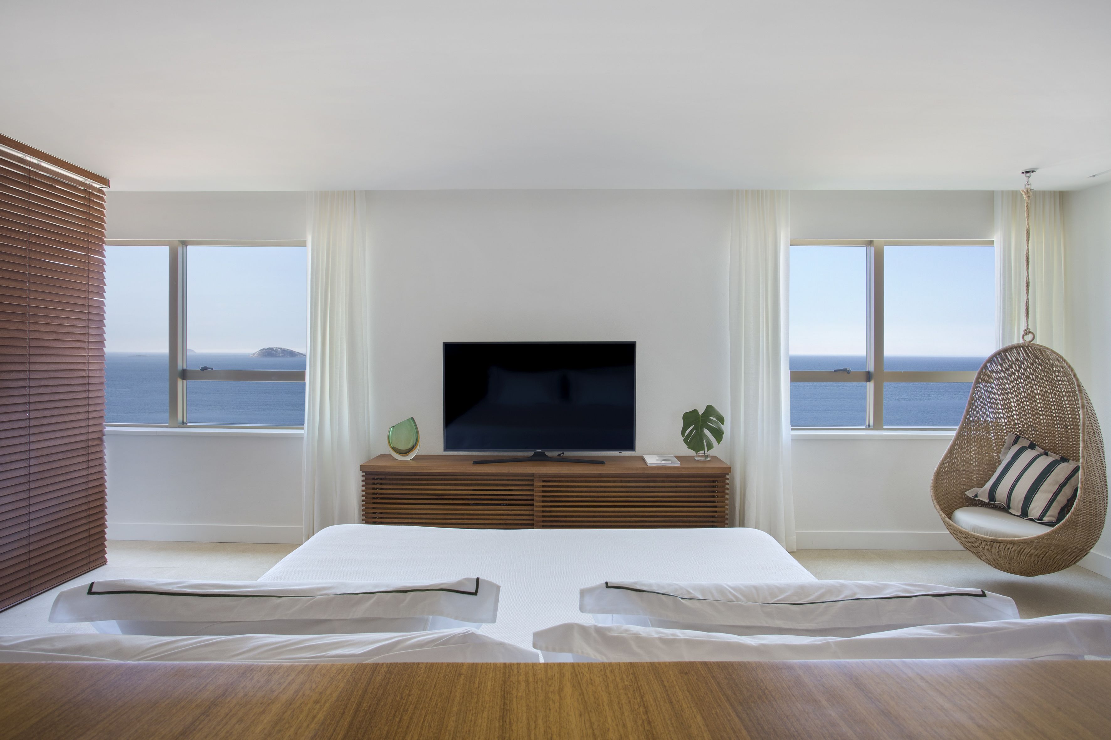 Un dormitorio moderno con un televisor grande, muebles de madera y vista al mar.