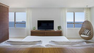 Un dormitorio moderno con un televisor grande, muebles de madera y vista al mar.