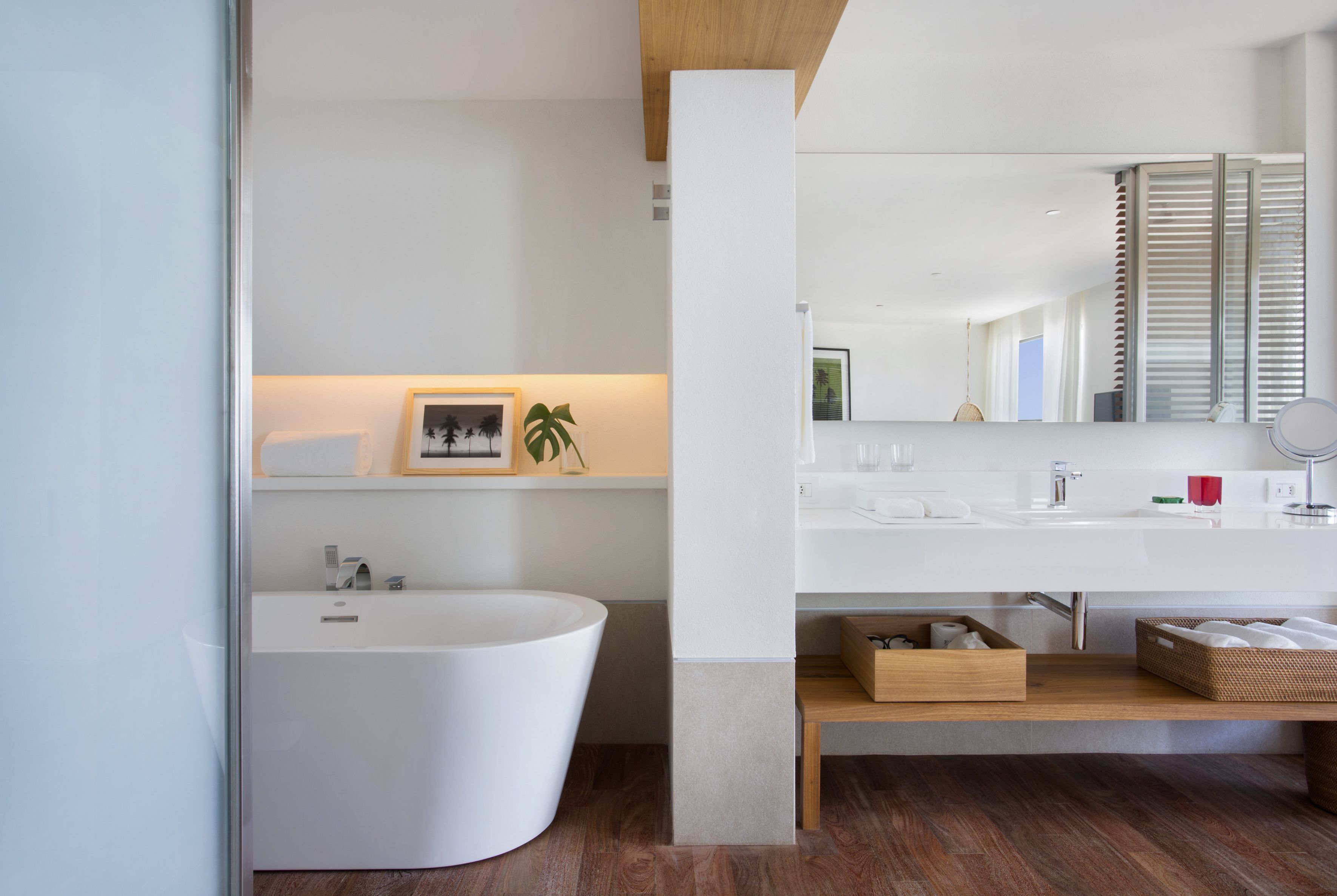A modern bathroom with a freestanding bathtub, a large mirror, and a wooden shelf.