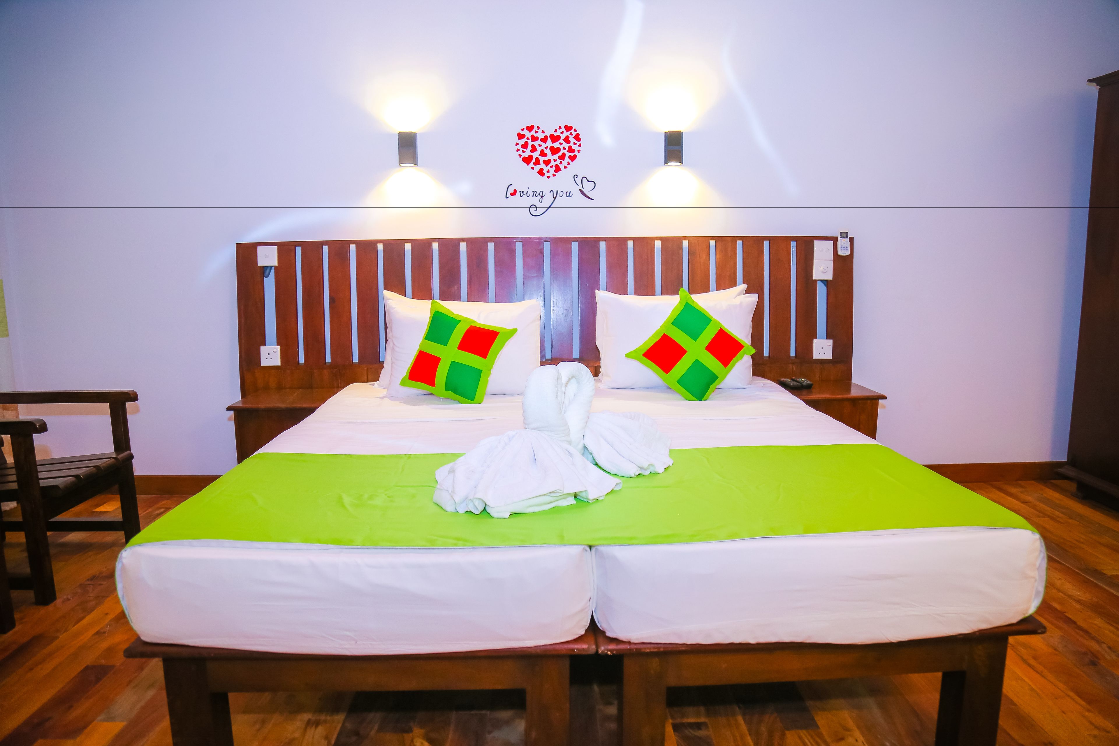 A double bed with green and white bedding, two pillows with red and green patterns, and a heart-shaped decoration on the wall.