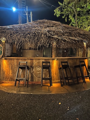 A rustic outdoor seating area with a thatched roof, wooden bar counter, and three bar stools. - Cozy Sea View Inn (Hikkaduwa)