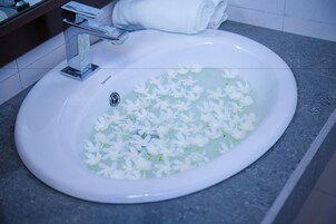 A bathroom sink with a white basin filled with water and white flowers.