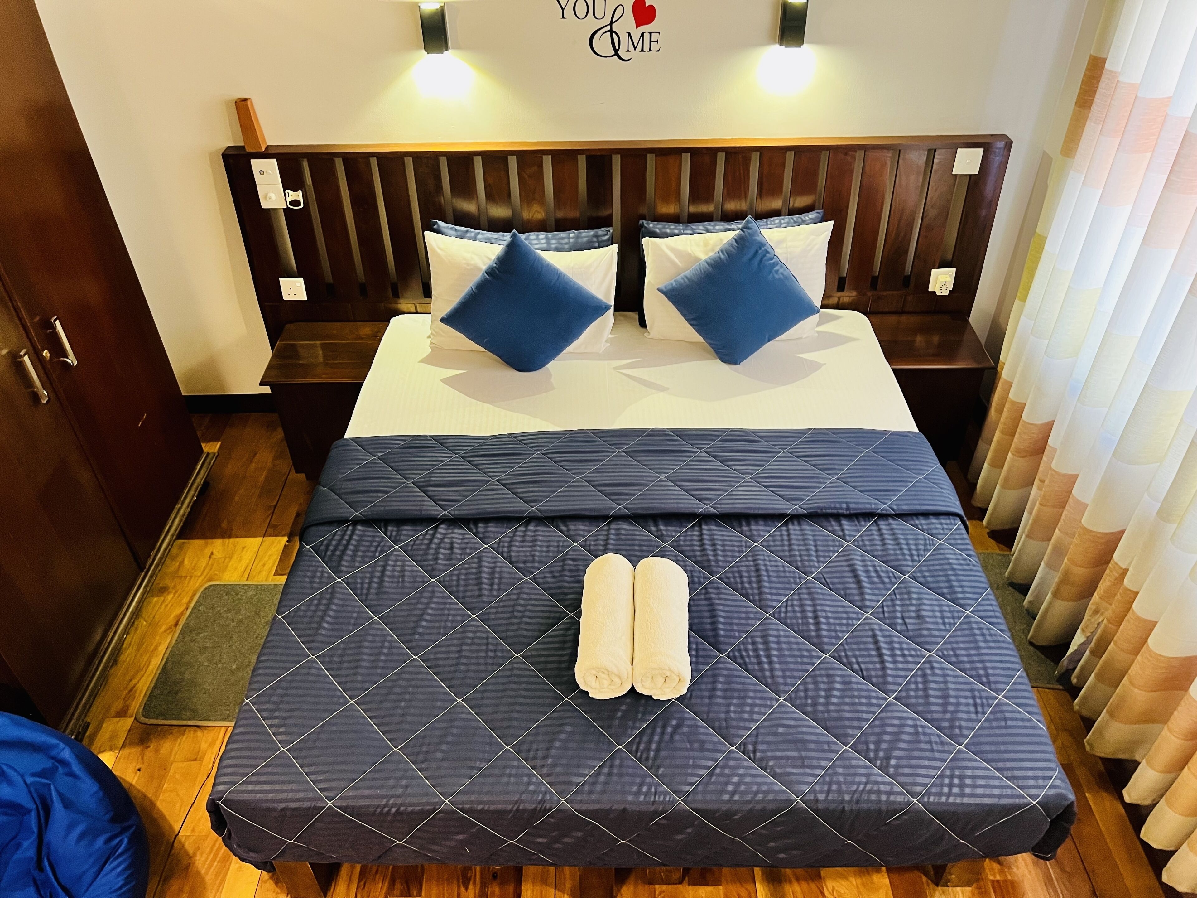 A neatly made bed with a dark quilt, two pillows, and two rolled towels.