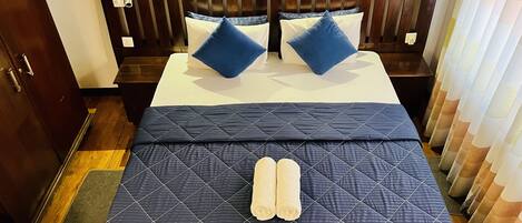 Cama bem arrumada com um edredom escuro, duas almofadas e duas toalhas enroladas.