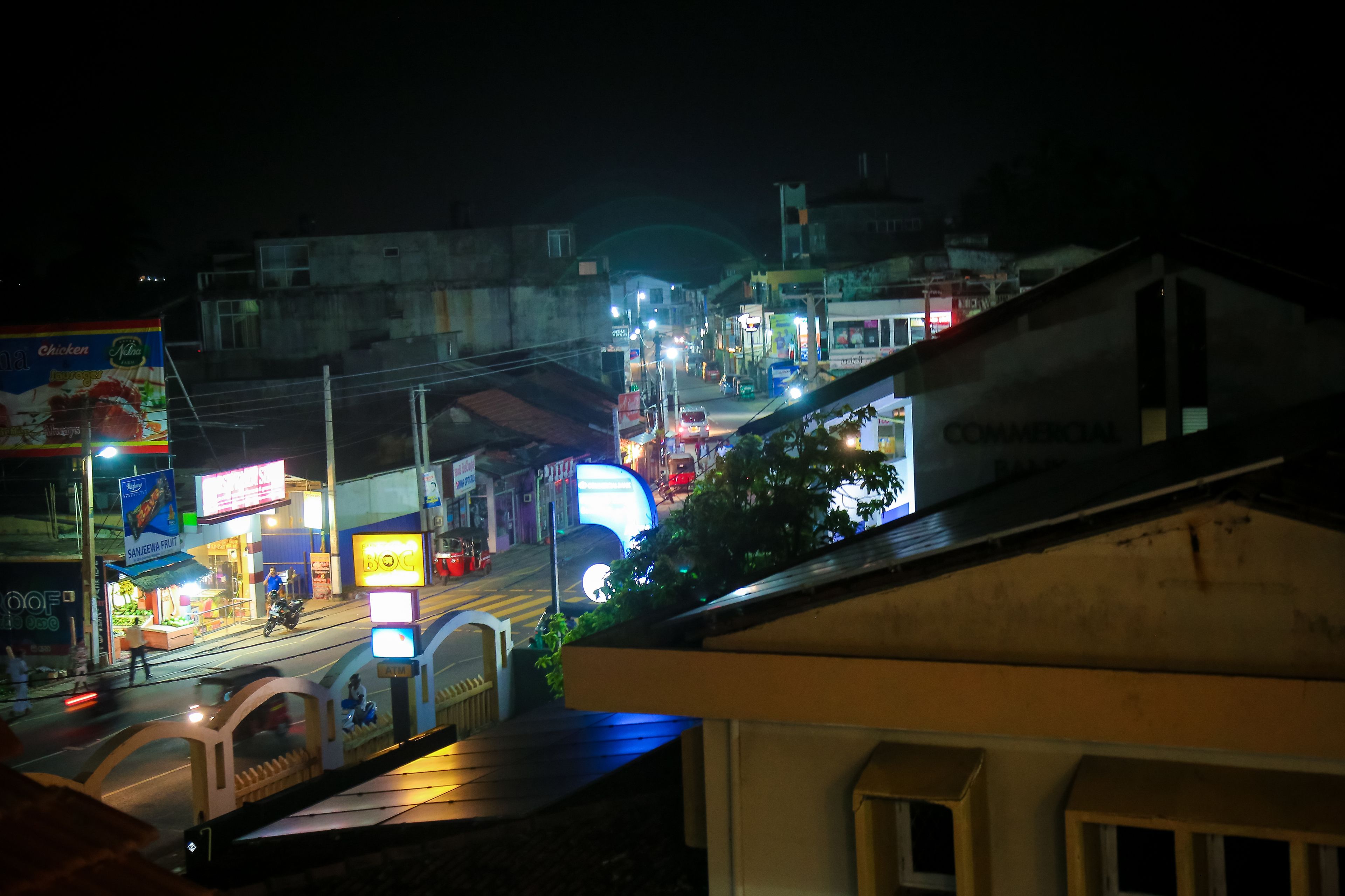 A nighttime street view with illuminated shops and a pedestrian bridge.