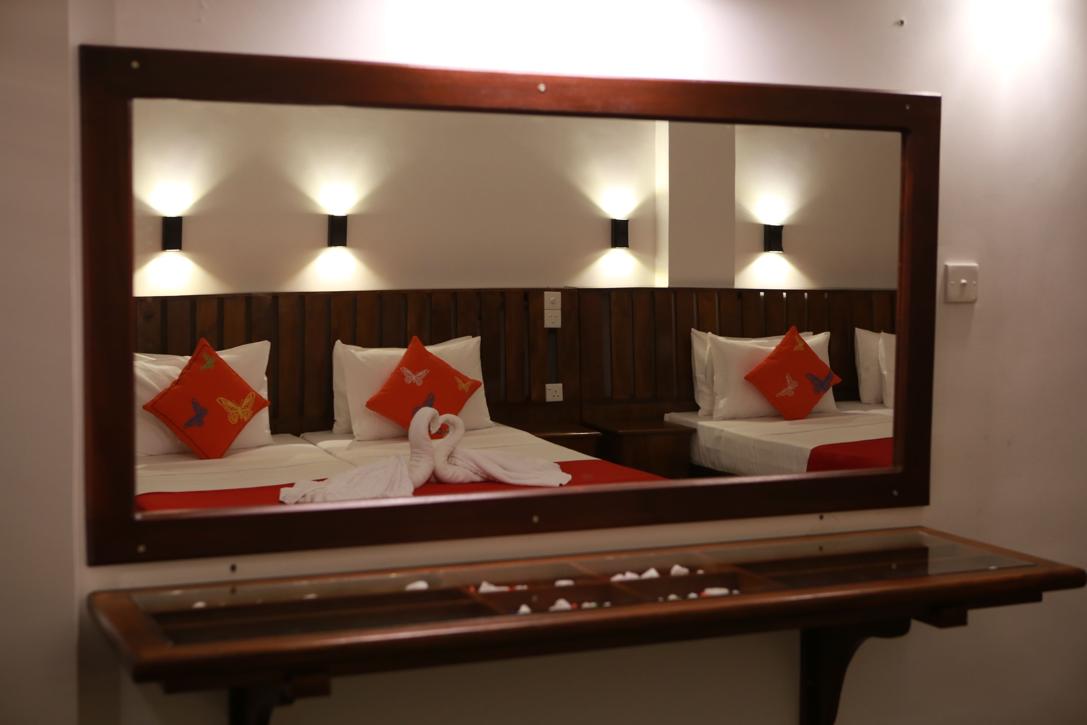 A hotel room with a large mirror, wooden headboard, and two beds with red pillows.