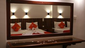 A hotel room with a large mirror, wooden headboard, and two beds with red pillows.
