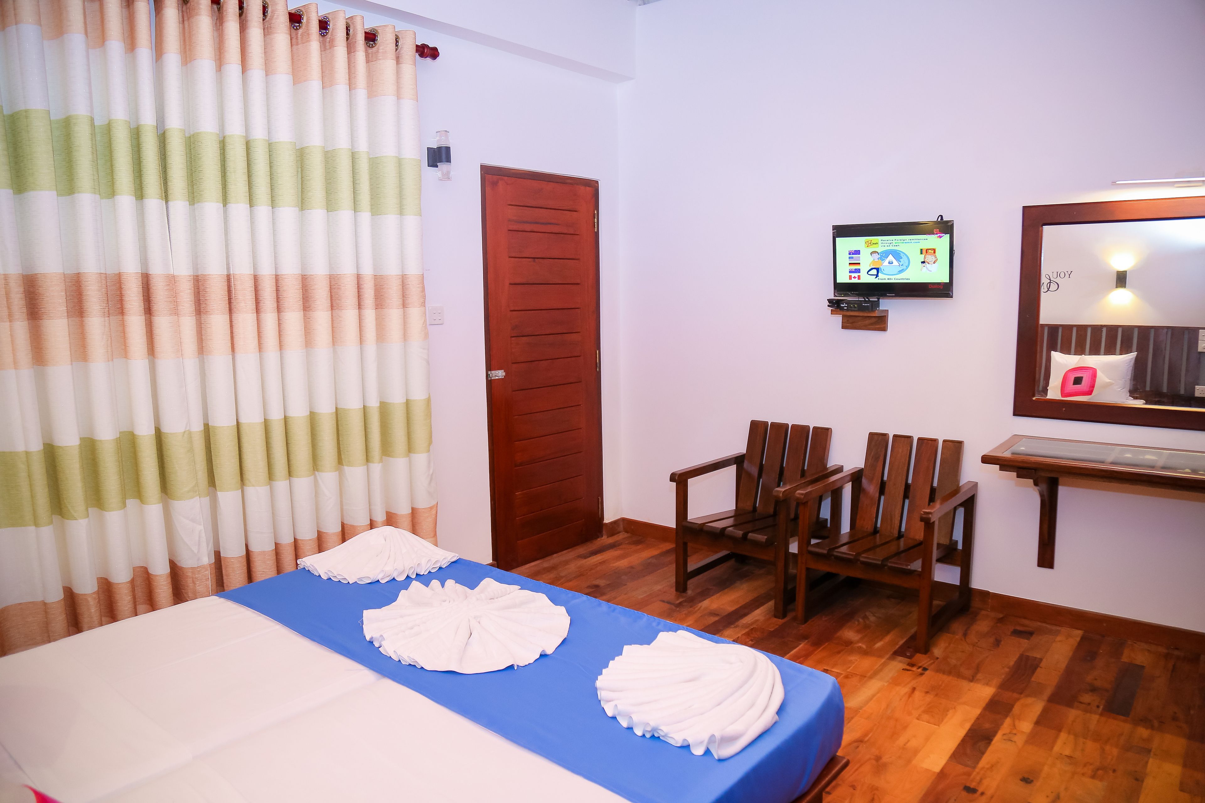 Habitación de hotel con una cama, televisor, una silla de madera y suelo de madera.