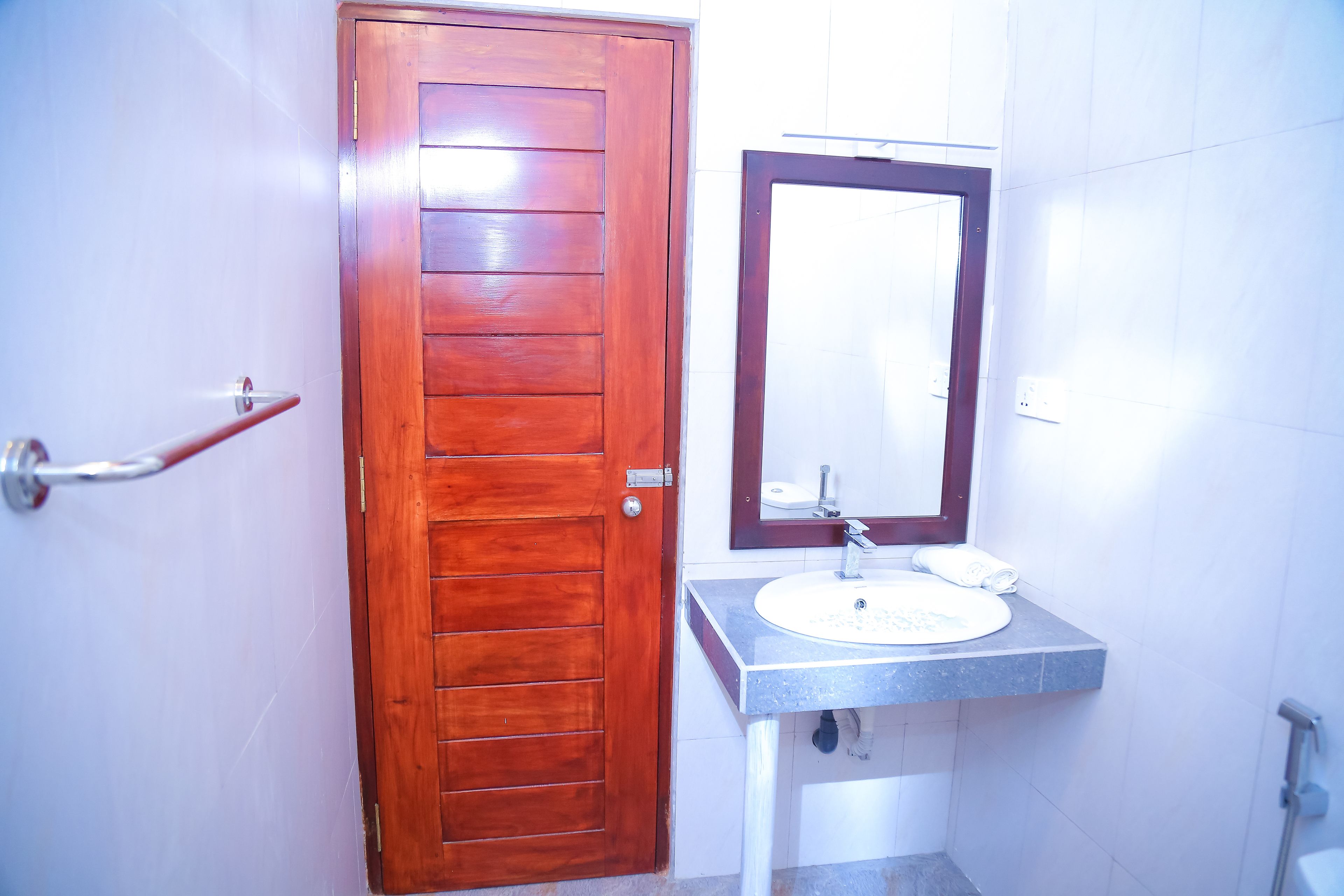 A bathroom with a wooden door, a sink with a mirror, and a towel rack.