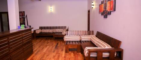 A wooden reception desk, a sofa, and a dining table in a room with wooden flooring and a sloped ceiling.
