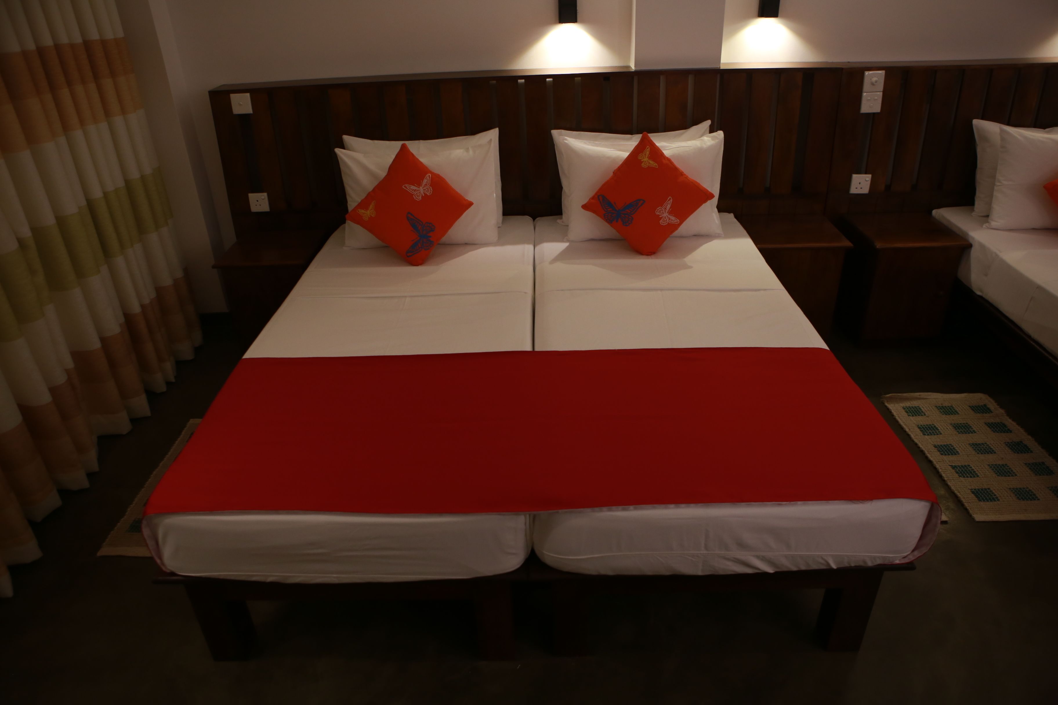 A double bed with a red bedspread and two pillows with butterfly designs.