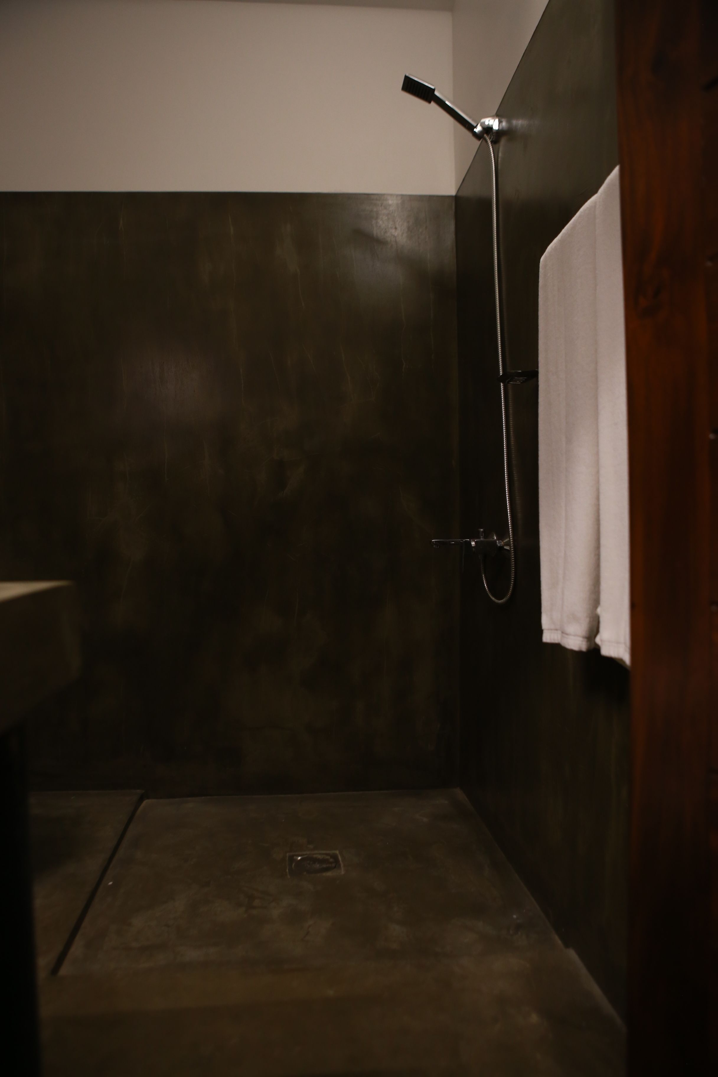 A small, dimly lit bathroom with a shower, a towel hanging on the wall, and a wooden door.