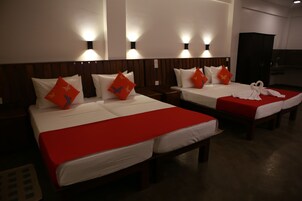 Habitación de hotel con dos camas, cada una con colcha roja y ropa de cama blanca. Hay luces fijadas a la pared sobre las camas y un armario oscuro al fondo.