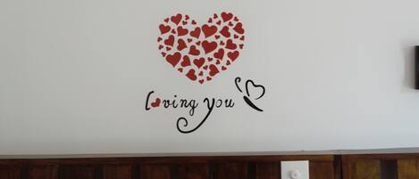 Una pared con un diseño en forma de corazón hecho con corazones más pequeños y el texto 'loving you' debajo.