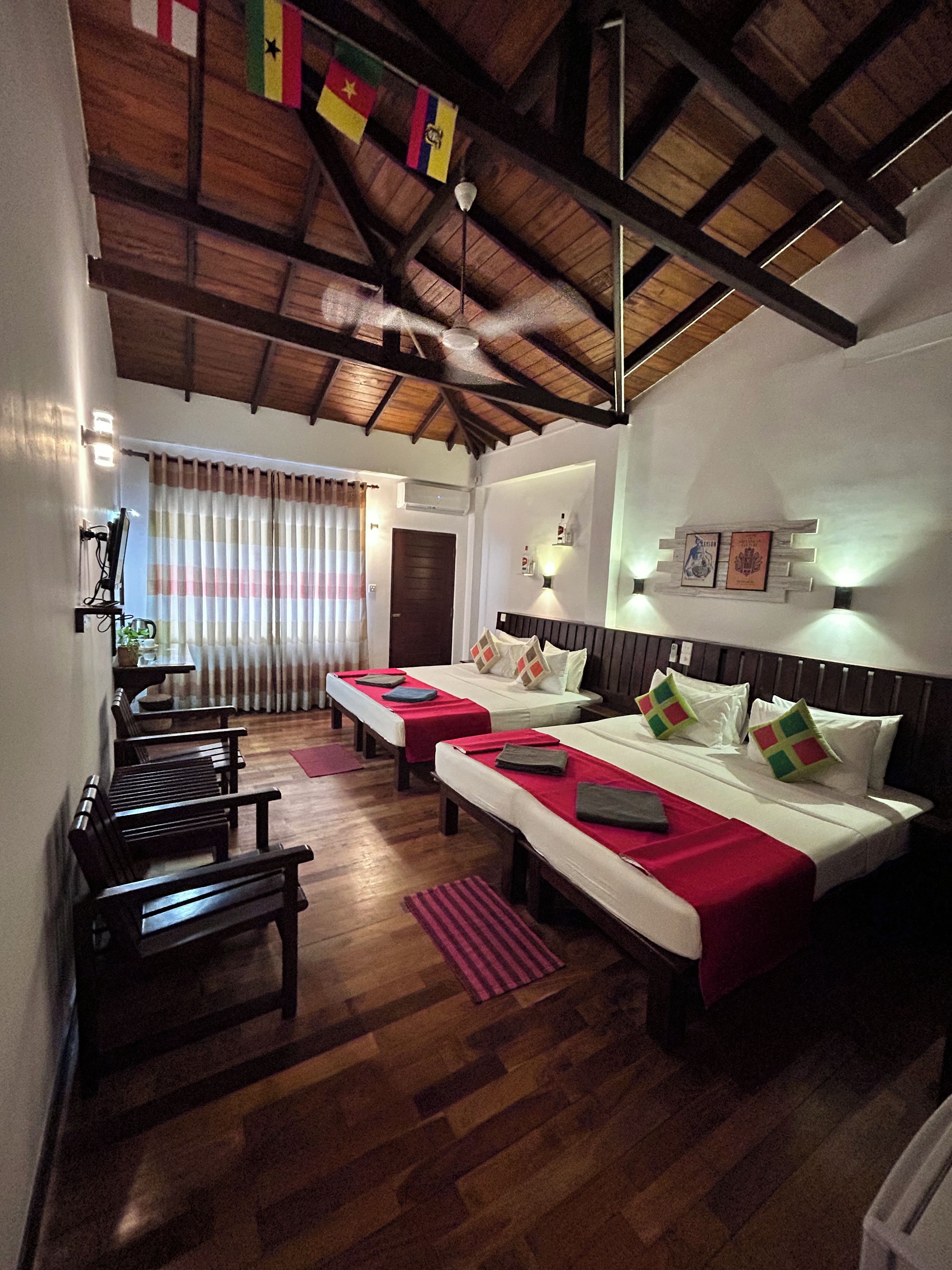 A hotel room with two beds, wooden flooring, a ceiling fan, and a view of the outdoors.