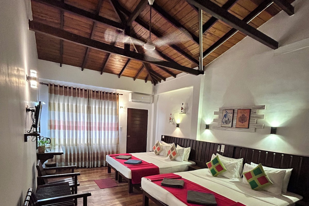 A hotel room with two beds, wooden flooring, a ceiling fan, and a view of the outdoors.