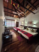Habitación de hotel con dos camas, suelo de madera, ventilador de techo y vistas al exterior.
