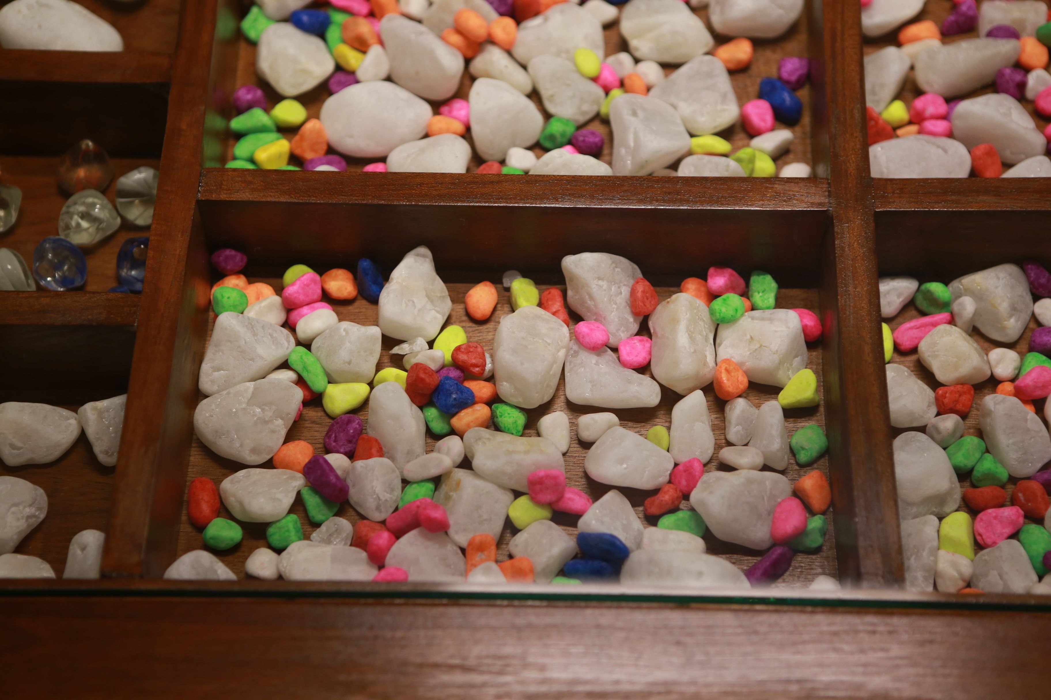 A display of variously colored pebbles and stones in wooden compartments.