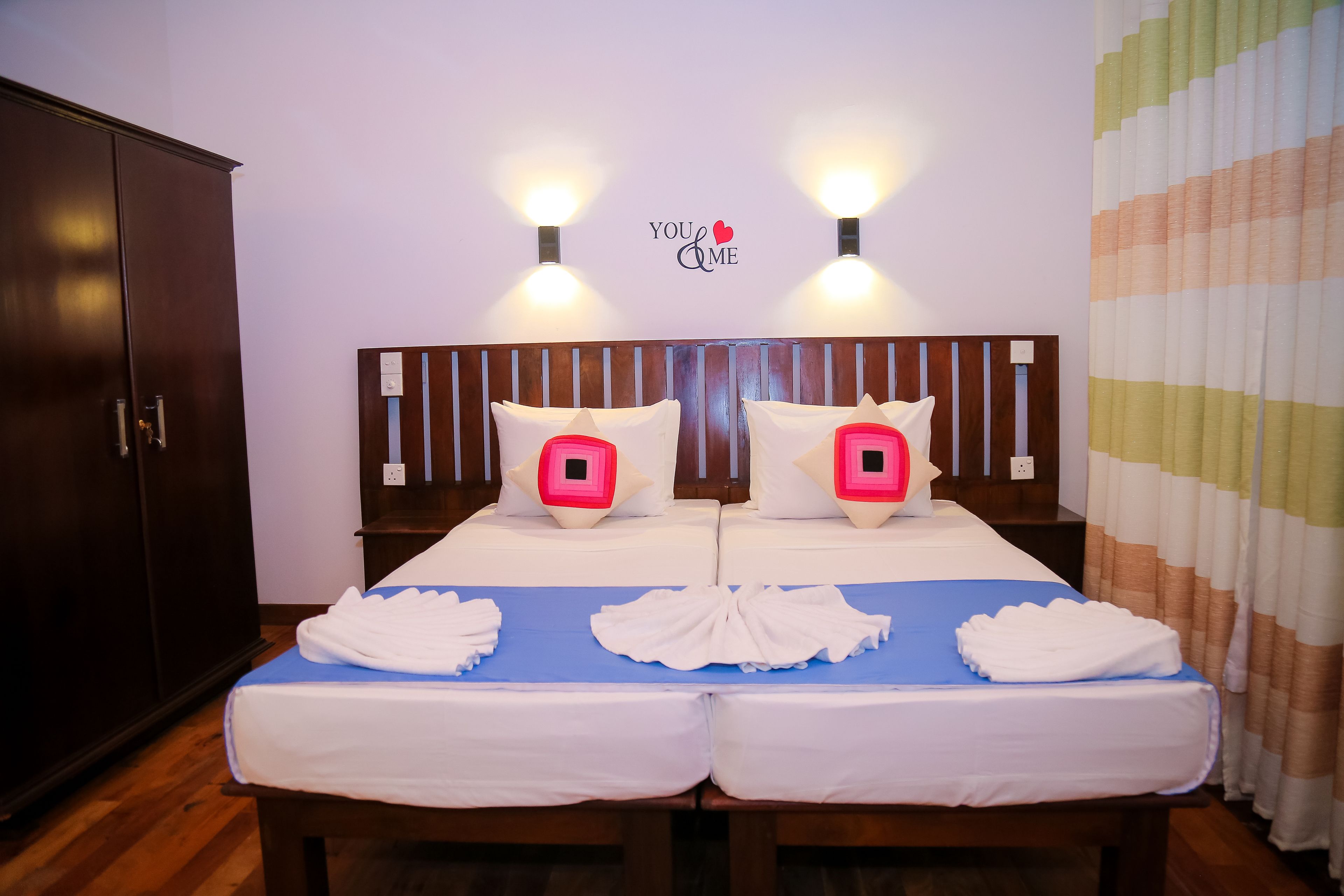 Un letto matrimoniale con copripiumino blu, due cuscini con dettagli rosa e un cartello con la scritta 'You & Me'.