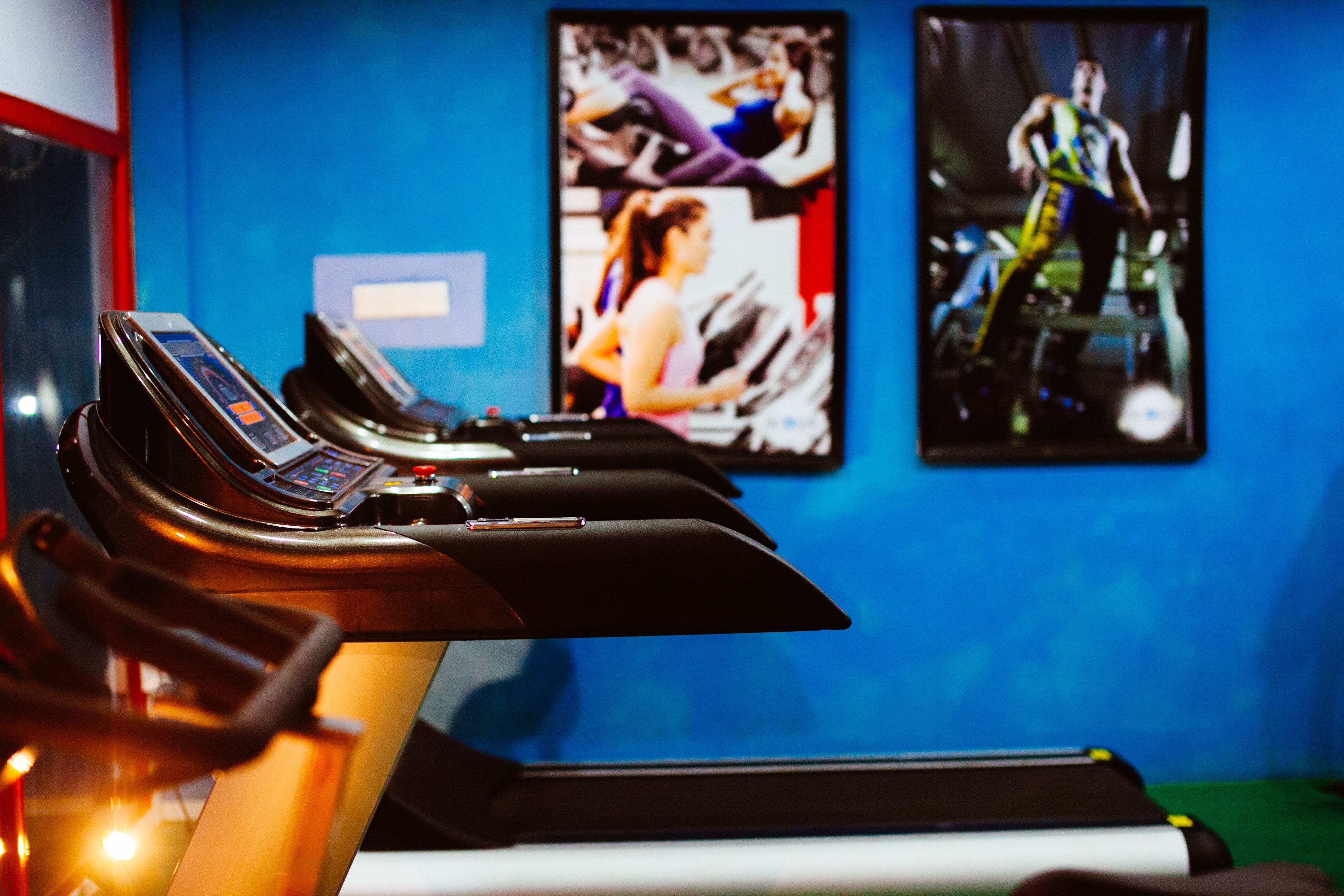 A treadmill in a gym with a blue wall and a poster of a person running.